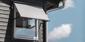 Kuva modernista talon ikkunasta ja vedenpoistoputkesta, jossa aurinkosuojaverho ja sateensuoja.